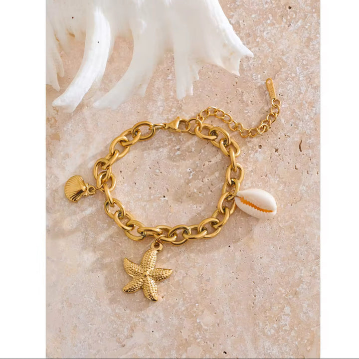 Gold chain bracelet with starfish and shell charms on a sandy background